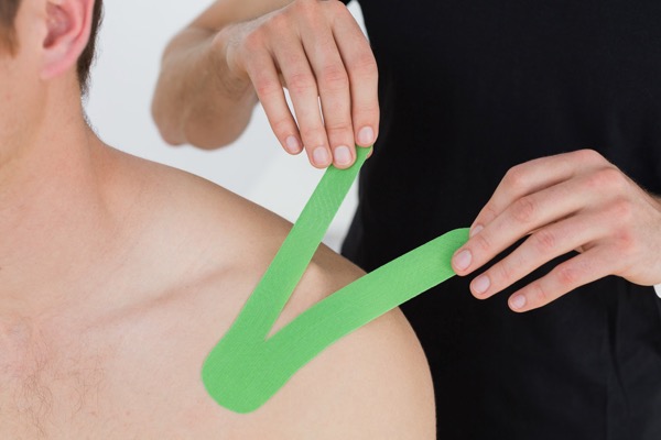 Sport injury treated by Hosford Health Clinic osteopath; osteopath putting green kinesio tape on a patient's shoulder
